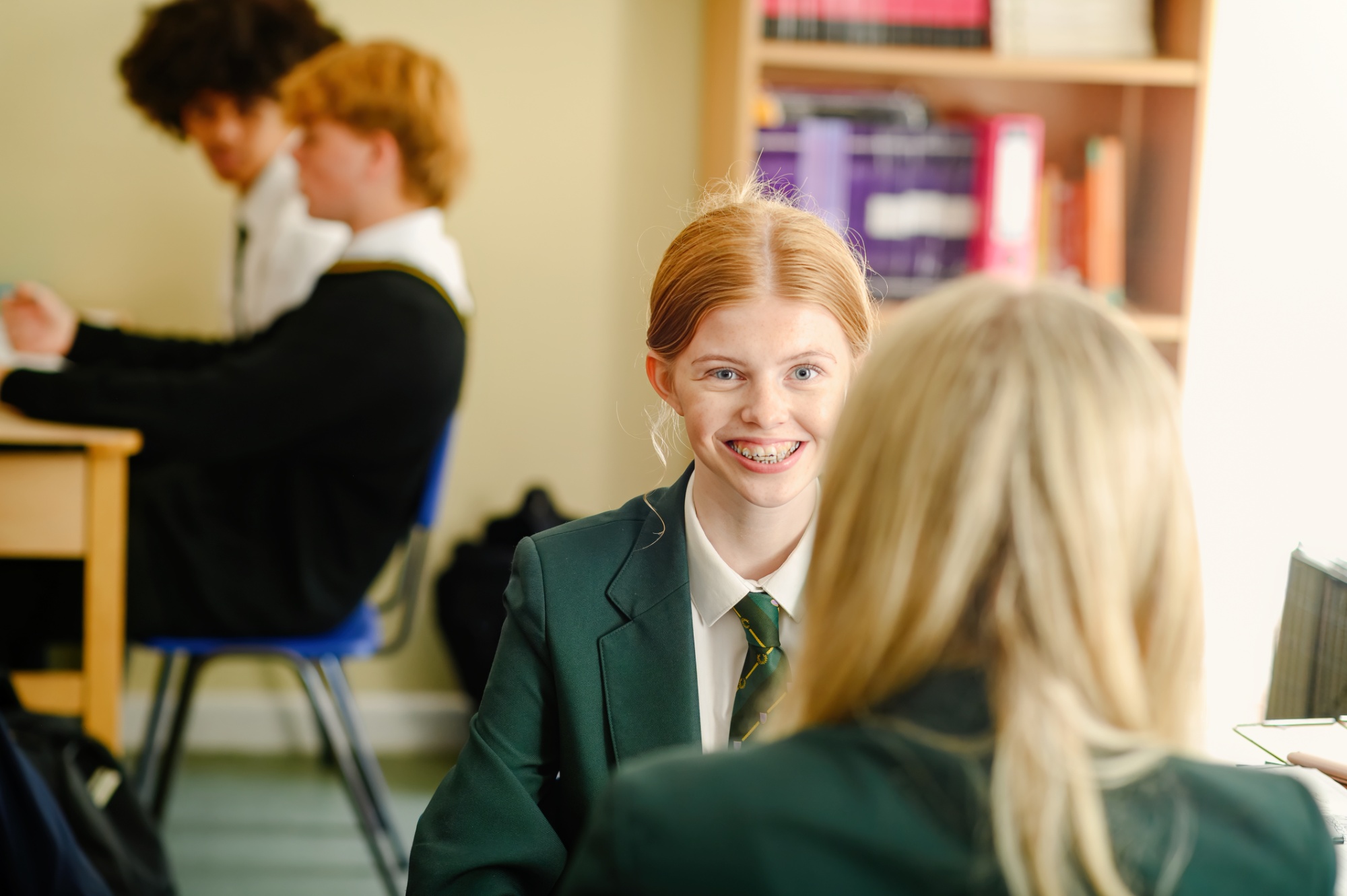 Two female students speak to each other while sat in a classroom.